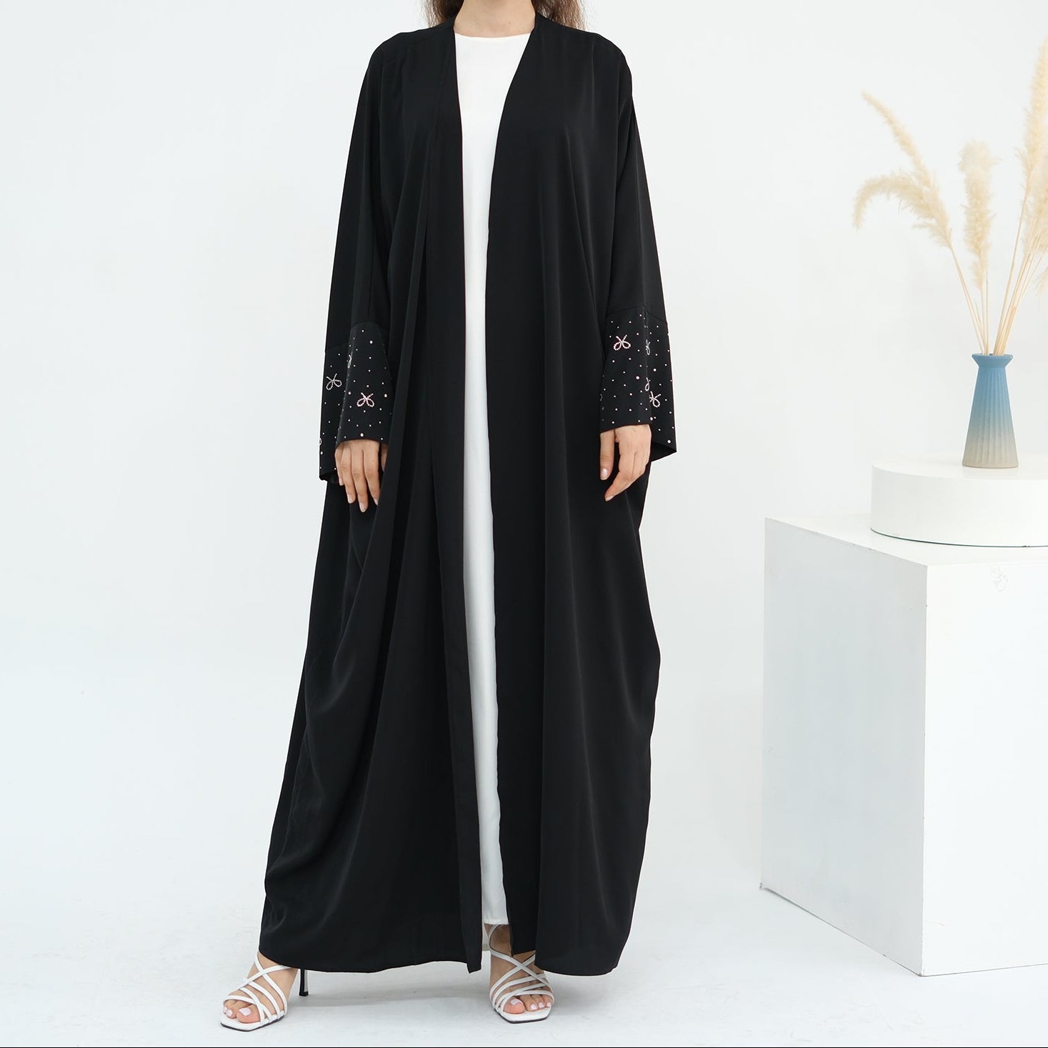 Woman wearing a black abaya with white stripes on a white background. AlLayaliEmbroideredOpenAbaya_Noor_GraceBlack1
