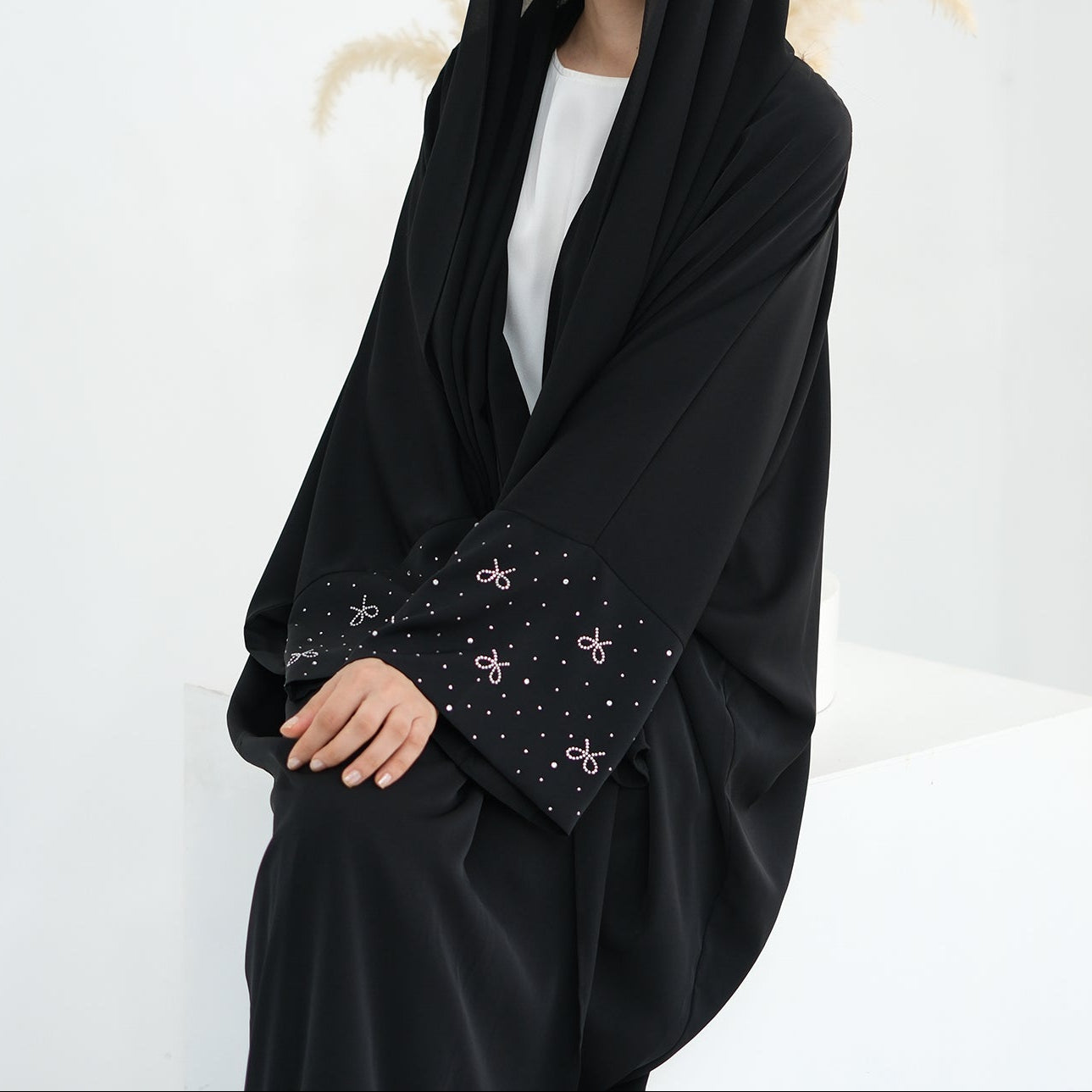 Woman wearing a black hijab with decorative trim on a white. AlLayaliEmbroideredOpenAbaya_Noor_GraceBlack10background