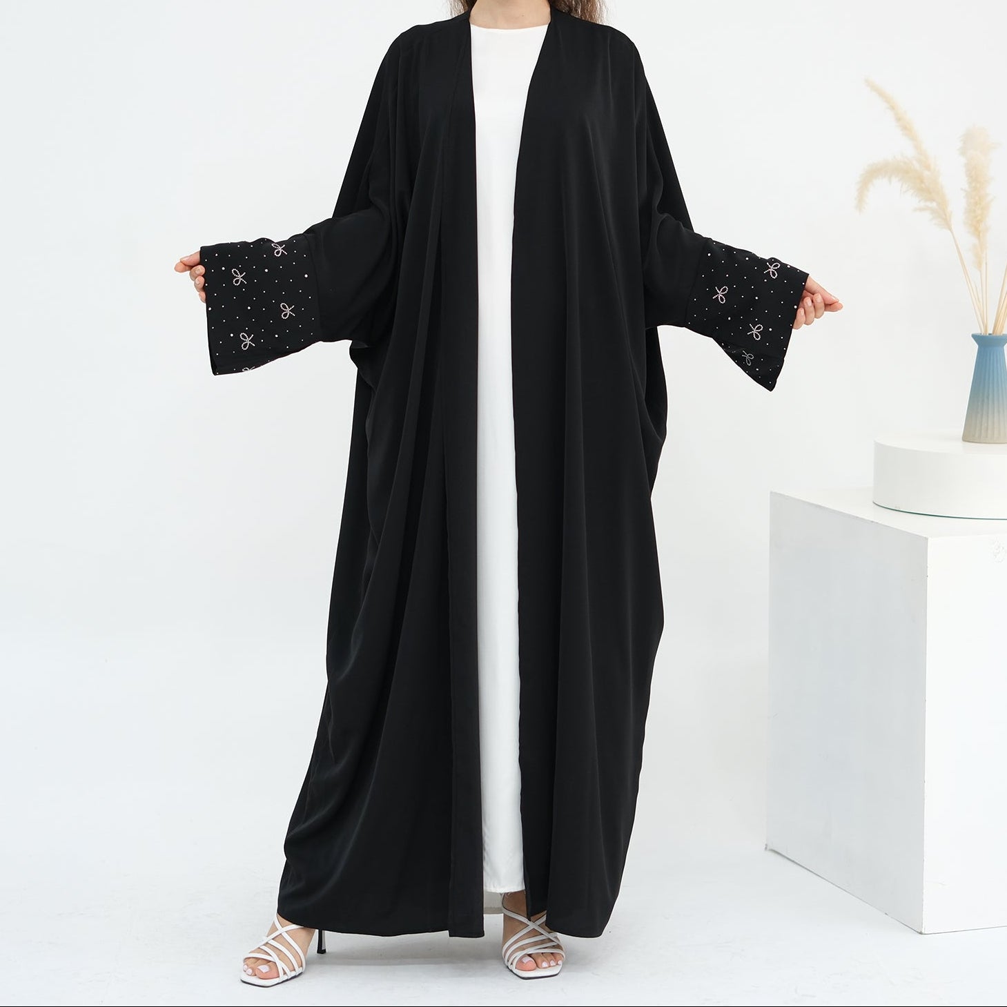 Woman wearing a black abaya with white background. AlLayaliEmbroideredOpenAbaya_Noor_GraceBlack2