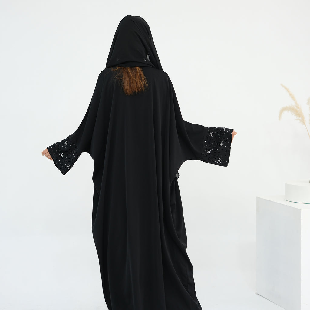Person wearing a black abaya with star patterns on a white background. AlLayaliEmbroideredOpenAbaya_Noor_GraceBlack9