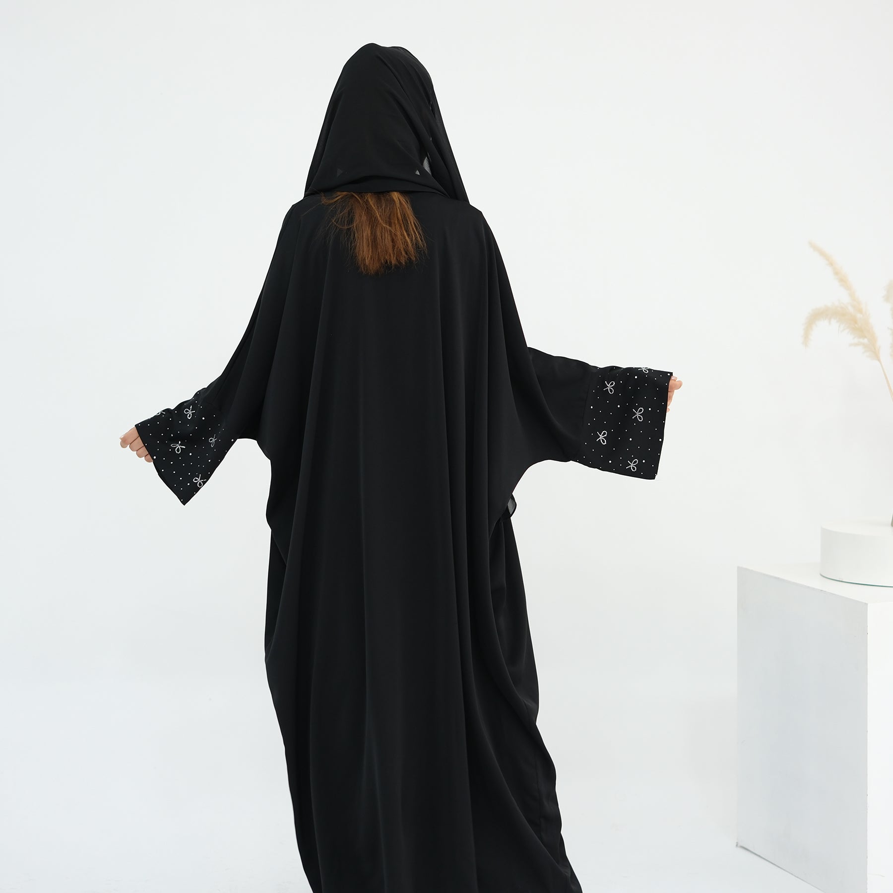 Person wearing a black abaya with star patterns on a white background. AlLayaliEmbroideredOpenAbaya_Noor_GraceBlack9