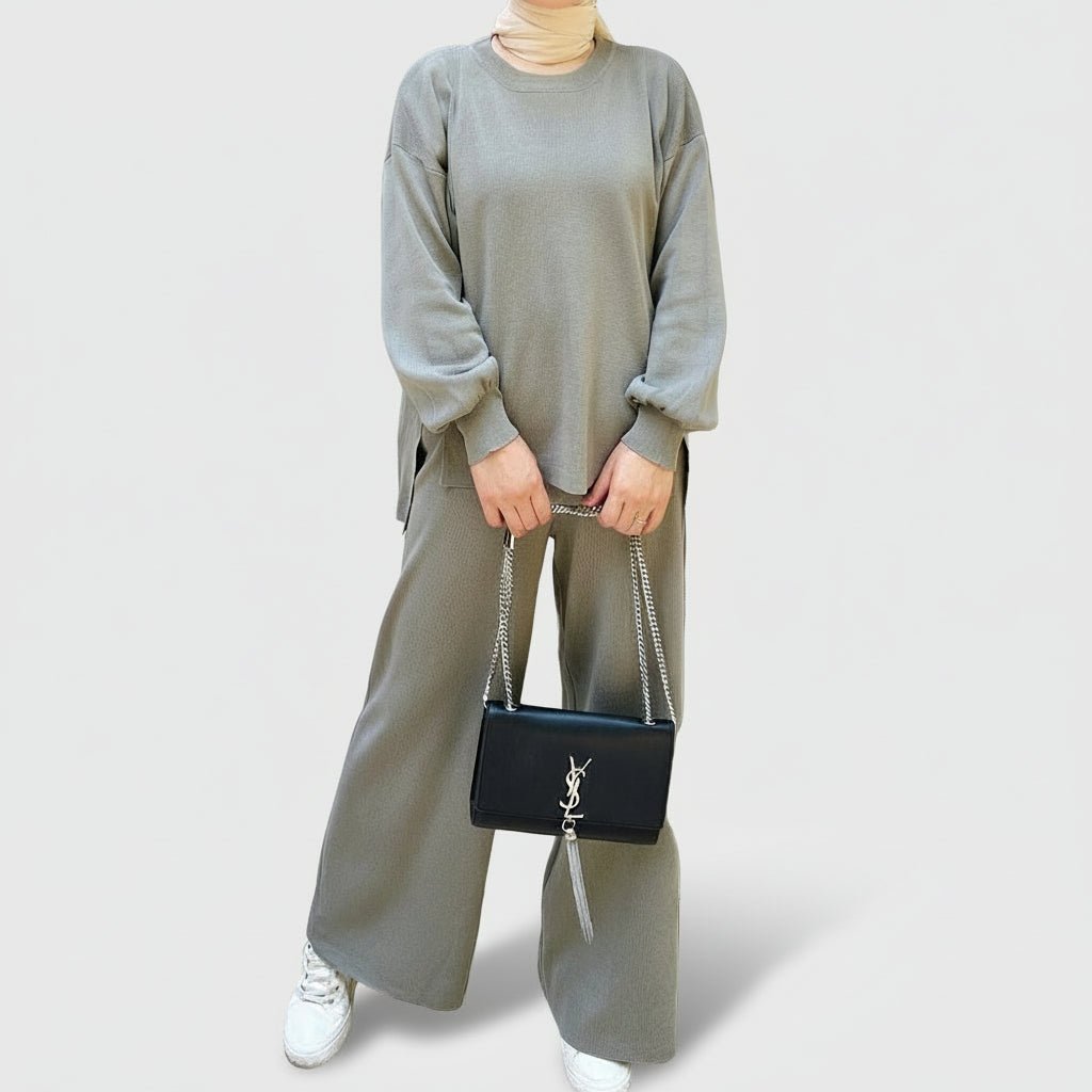 Person wearing a gray outfit holding a black handbag in an outdoor setting. AlSaharKnitted2-PieceSweater_PantsSet_Gray1 - Noor & Grace