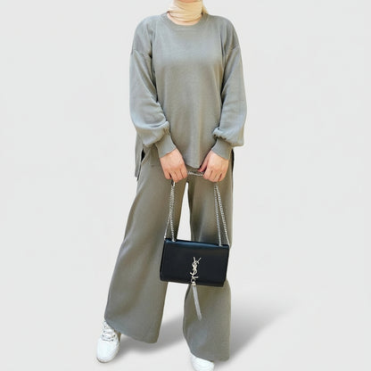 Person wearing a gray outfit holding a black handbag in an outdoor setting. AlSaharKnitted2-PieceSweater_PantsSet_Gray1 - Noor & Grace