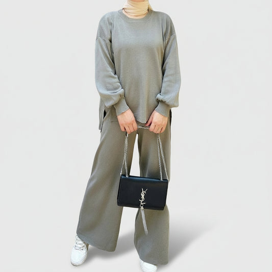 Person wearing a gray outfit holding a black handbag in an outdoor setting. AlSaharKnitted2-PieceSweater_PantsSet_Gray1 - Noor & Grace