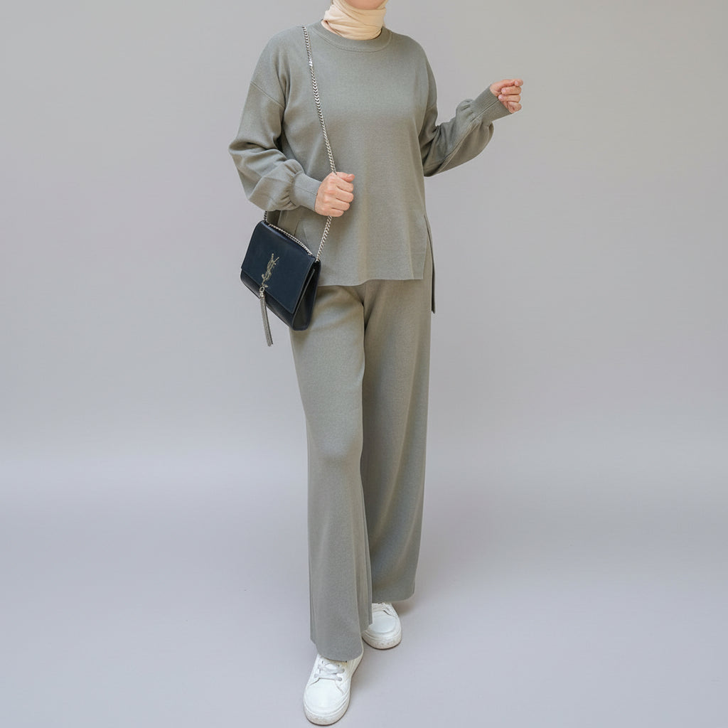 Person wearing a gray outfit holding a black handbag in an outdoor setting. AlSaharKnitted2-PieceSweater_PantsSet_Gray1 - Noor & Grace