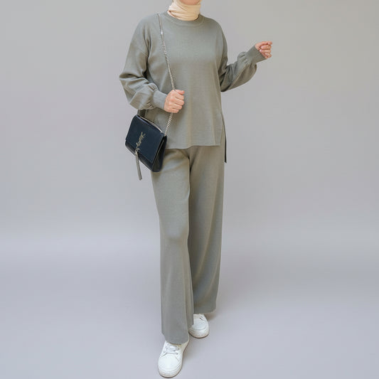 Person wearing a gray outfit holding a black handbag in an outdoor setting. AlSaharKnitted2-PieceSweater_PantsSet_Gray1 - Noor & Grace