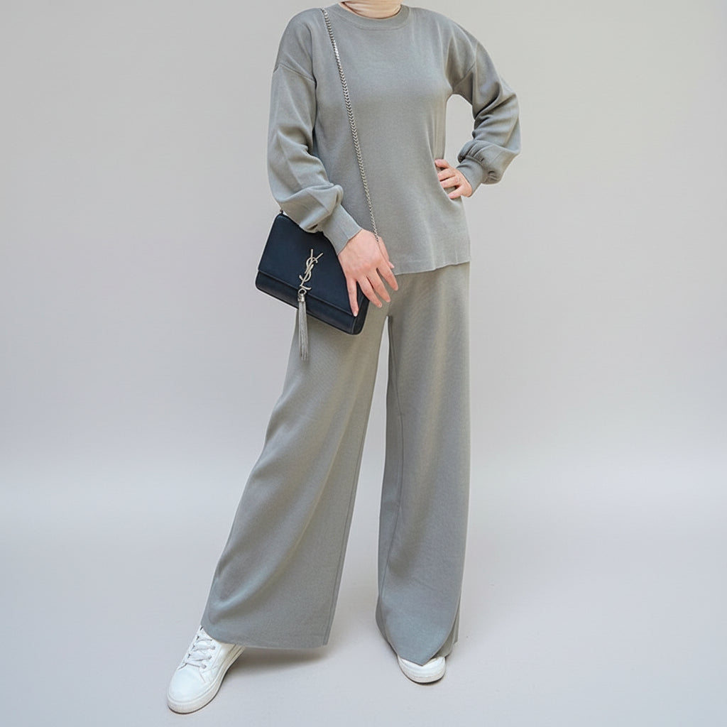 Person wearing a gray outfit holding a black handbag in an outdoor setting. AlSaharKnitted2-PieceSweater_PantsSet_Gray1 - Noor & Grace