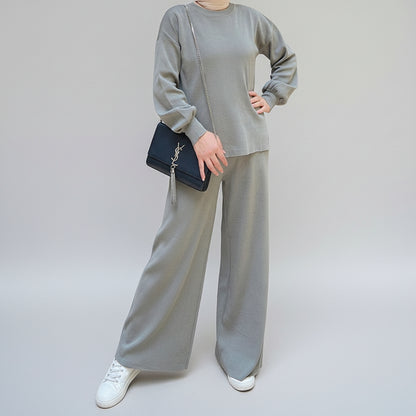Person wearing a gray outfit holding a black handbag in an outdoor setting. AlSaharKnitted2-PieceSweater_PantsSet_Gray1 - Noor & Grace