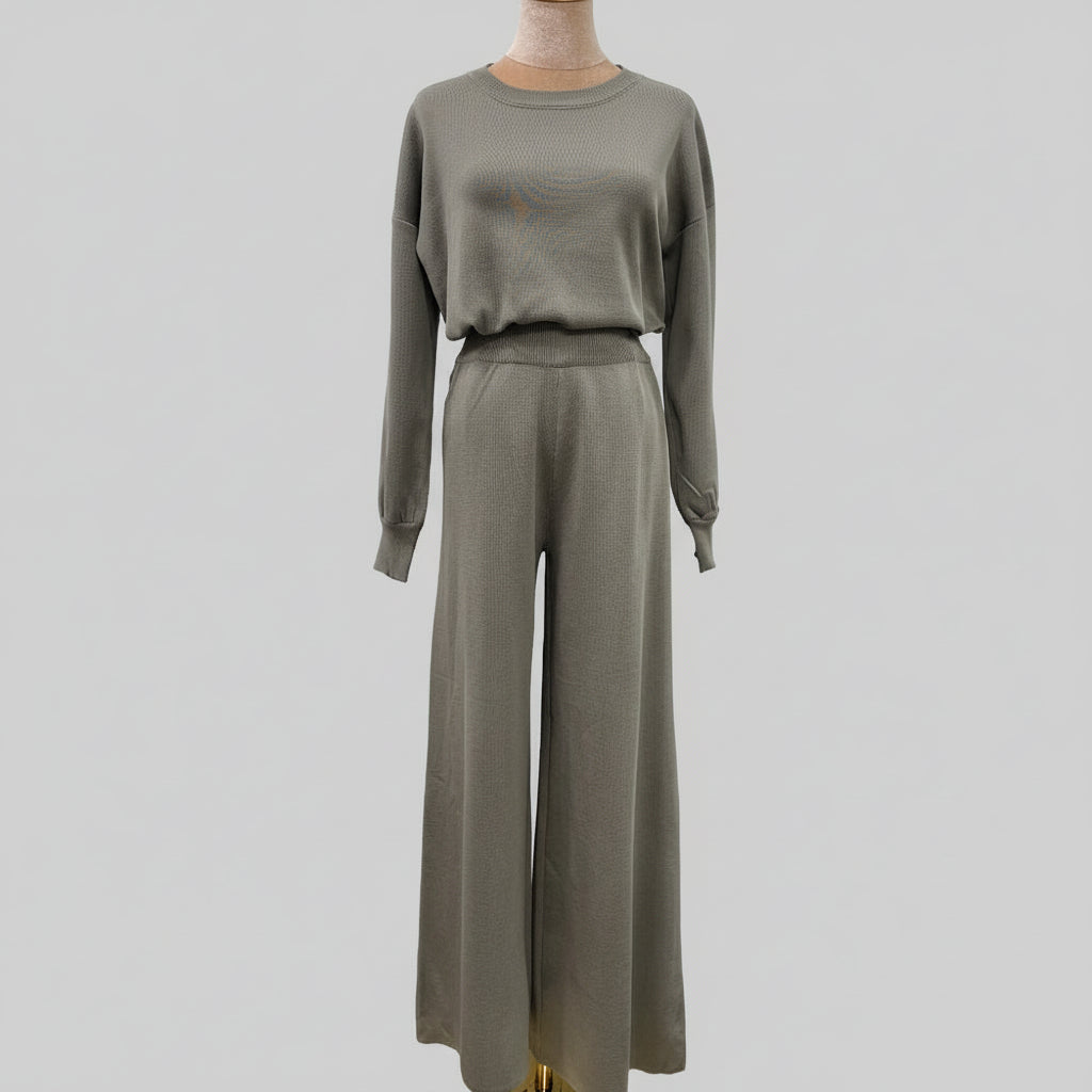 Person wearing a gray outfit holding a black handbag in an outdoor setting. AlSaharKnitted2-PieceSweater_PantsSet_Gray1 - Noor & Grace