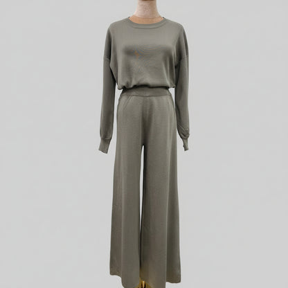 Person wearing a gray outfit holding a black handbag in an outdoor setting. AlSaharKnitted2-PieceSweater_PantsSet_Gray1 - Noor & Grace