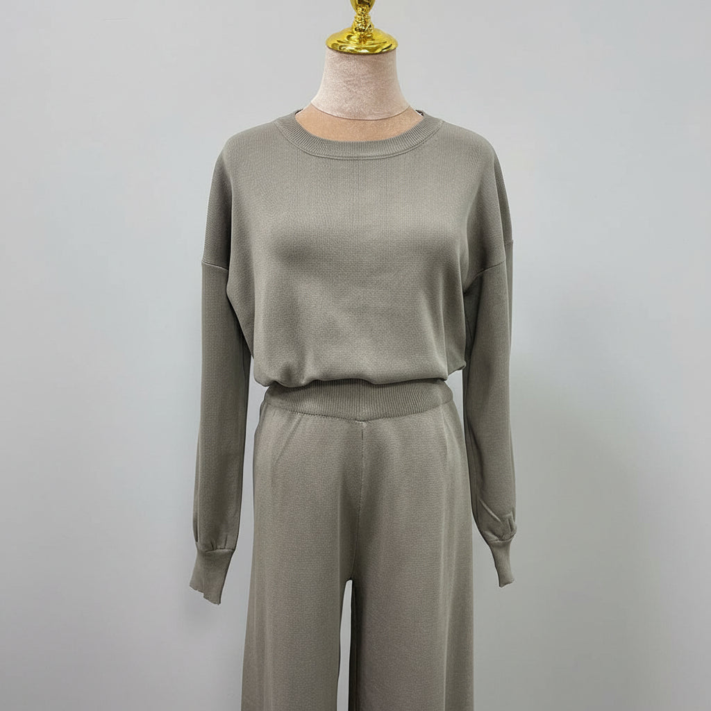 Person wearing a gray outfit holding a black handbag in an outdoor setting. AlSaharKnitted2-PieceSweater_PantsSet_Gray1 - Noor & Grace