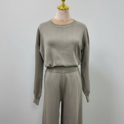 Person wearing a gray outfit holding a black handbag in an outdoor setting. AlSaharKnitted2-PieceSweater_PantsSet_Gray1 - Noor & Grace