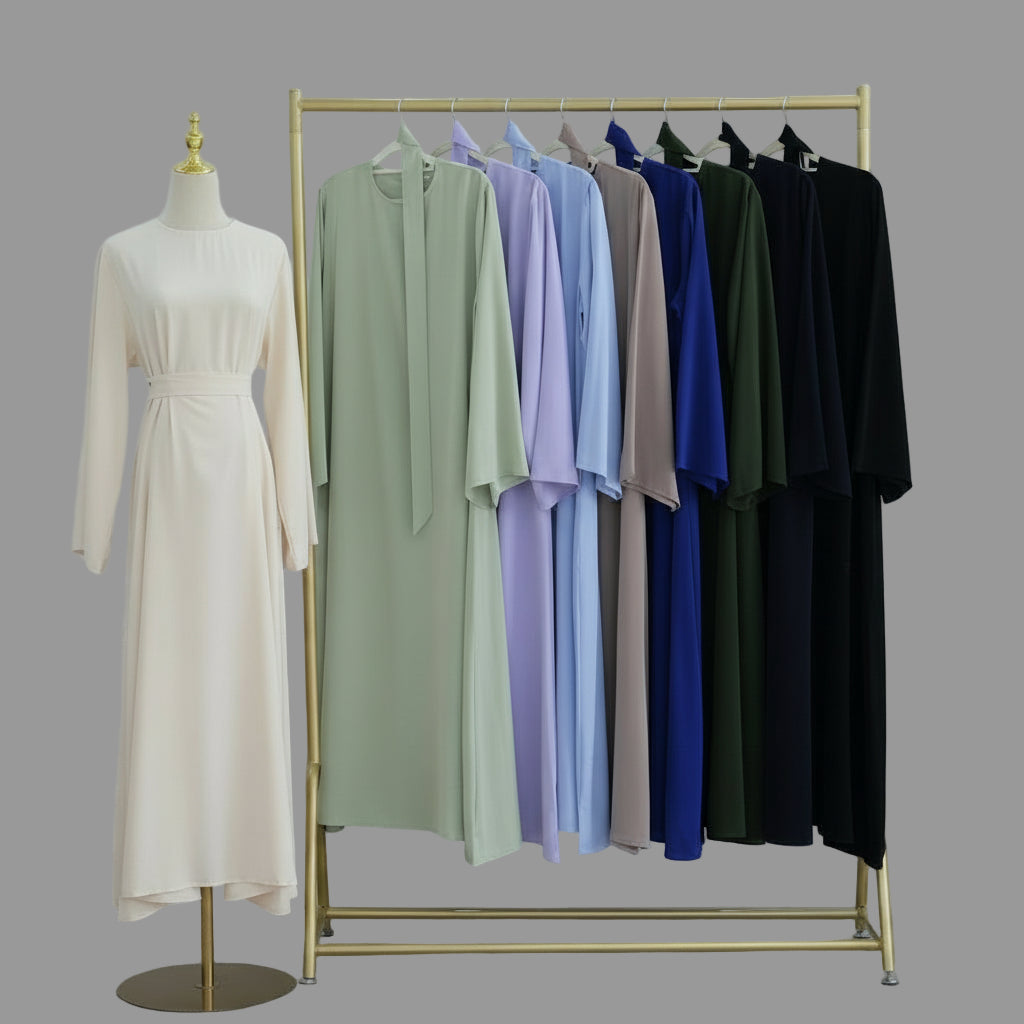 Mannequin with a beige dress and a rack of colorful dresses against a white wall. AsasAbayaInnerDress_Noor_Grace1 - Noor & Grace