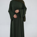 Person wearing a dark green abaya with a matching hijab on a light gray background