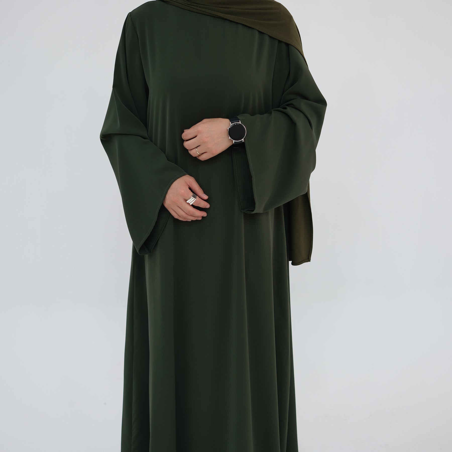 Person wearing a dark green abaya with a matching hijab on a light gray background