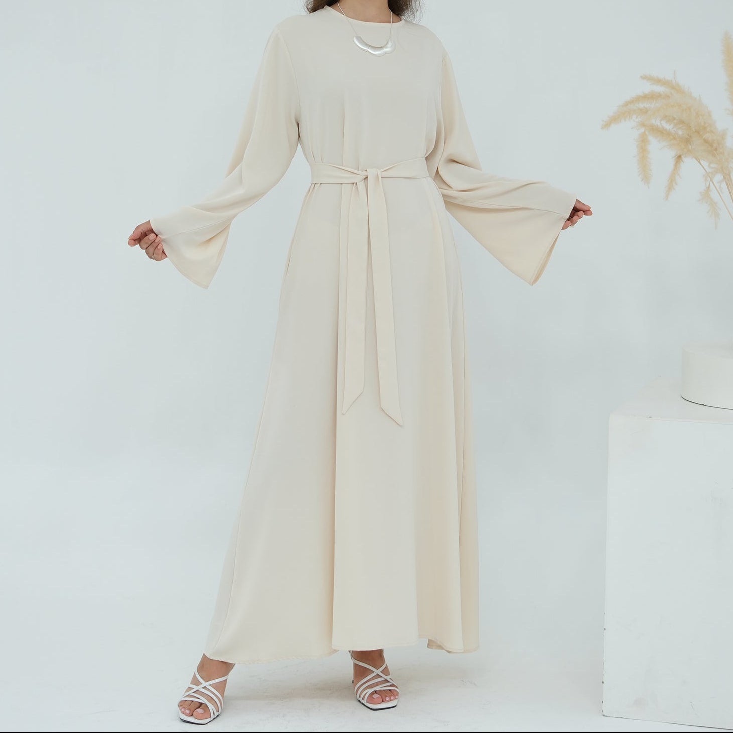 Woman wearing a long beige dress against a white background