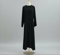 Black dress on a mannequin against a white paneled wall. AsasAbayaInnerDress_Noor_GraceBlack2 - Noor & Grace