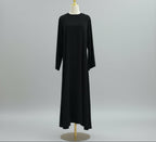 Black dress on a mannequin against a white paneled wall. AsasAbayaInnerDress_Noor_GraceBlack2 - Noor & Grace