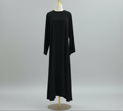 Black dress on a mannequin against a white paneled wall. AsasAbayaInnerDress_Noor_GraceBlack2 - Noor & Grace