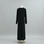 Black dress on a mannequin against a white paneled wall. AsasAbayaInnerDress_Noor_GraceBlack1 - Noor & Grace