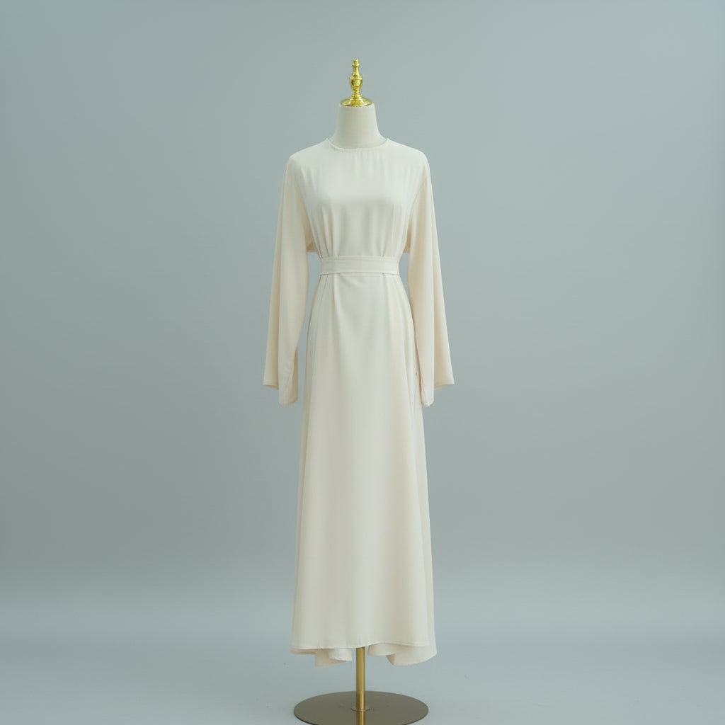 Beige dress on a mannequin against a white paneled wall. AsasAbayaInnerDress_Noor_Grace Beige - Noor & Grae