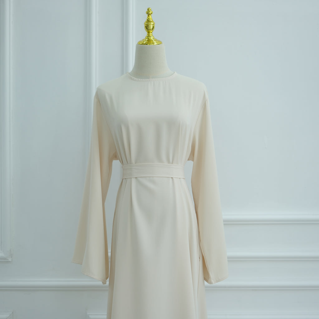 Beige dress on a mannequin against a white wall. AsasAbayaInnerDress_Noor_Grace Beige - Noor & Grace