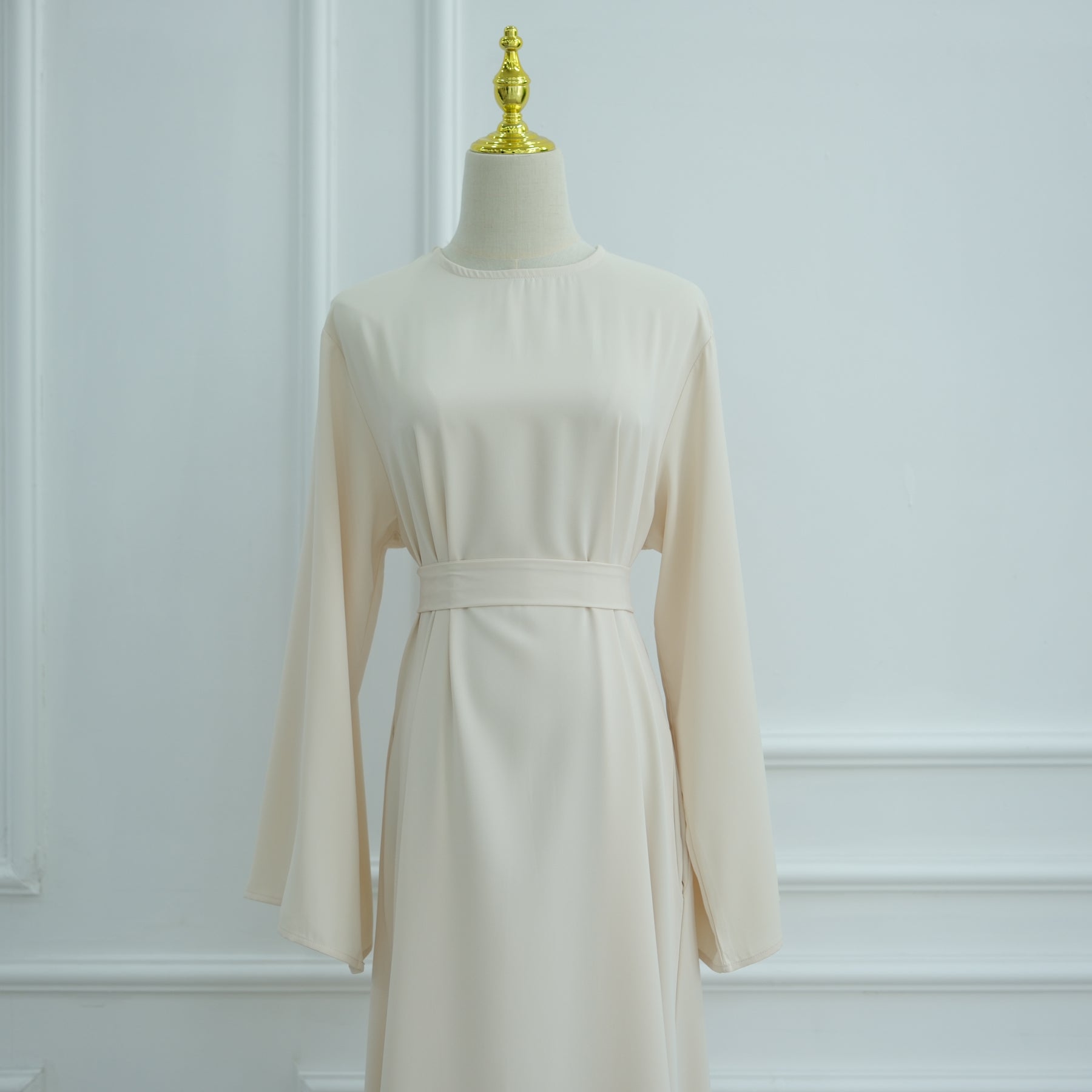 Beige dress on a mannequin against a white wall. AsasAbayaInnerDress_Noor_Grace Beige - Noor & Grace