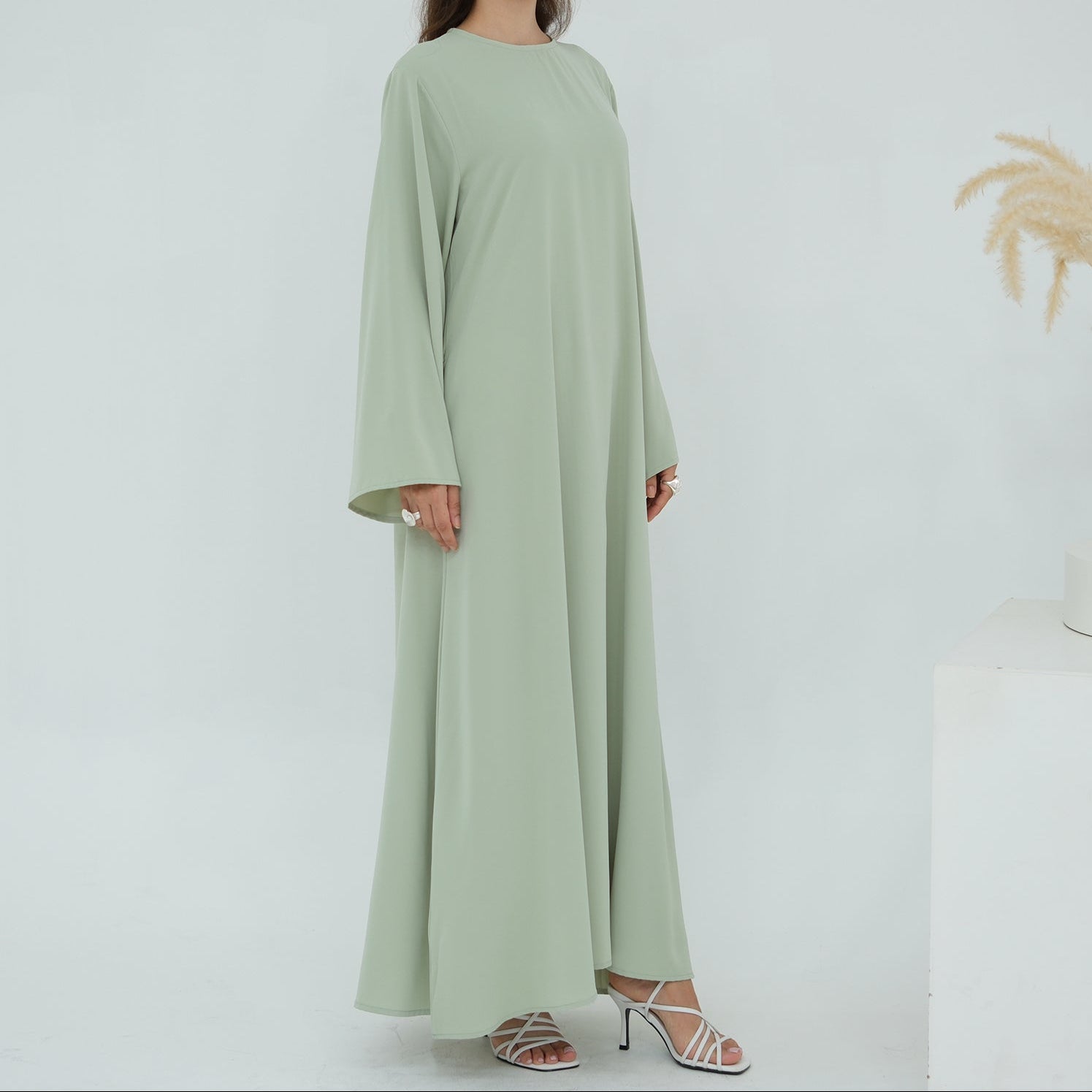 Woman wearing a long light green dress against a white background