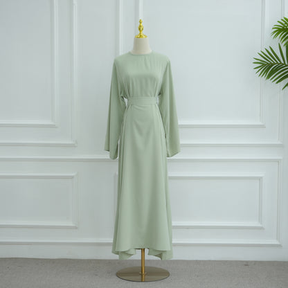 Green dress on a mannequin against a white paneled wall. AsasAbayaInnerDress_Noor_GraceGreen - Noor & Grace