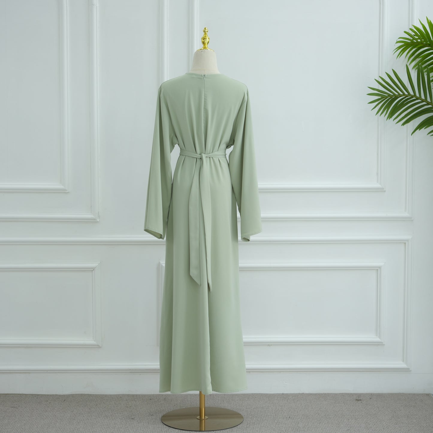 Green dress on a mannequin against a white paneled wall. AsasAbayaInnerDress_Noor_GraceGreen - Noor & Grace