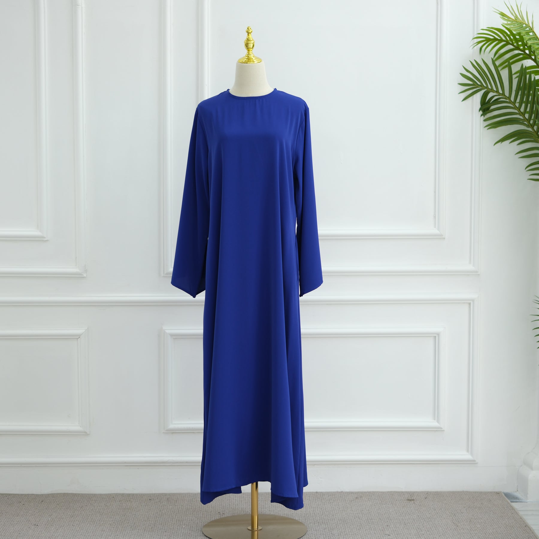 Blue dress on a mannequin against a white paneled wall. AsasAbayaInnerDress_Noor_GraceRoyalBlue - Noor & Grace