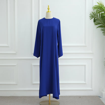 Blue dress on a mannequin against a white paneled wall. AsasAbayaInnerDress_Noor_GraceRoyalBlue - Noor & Grace
