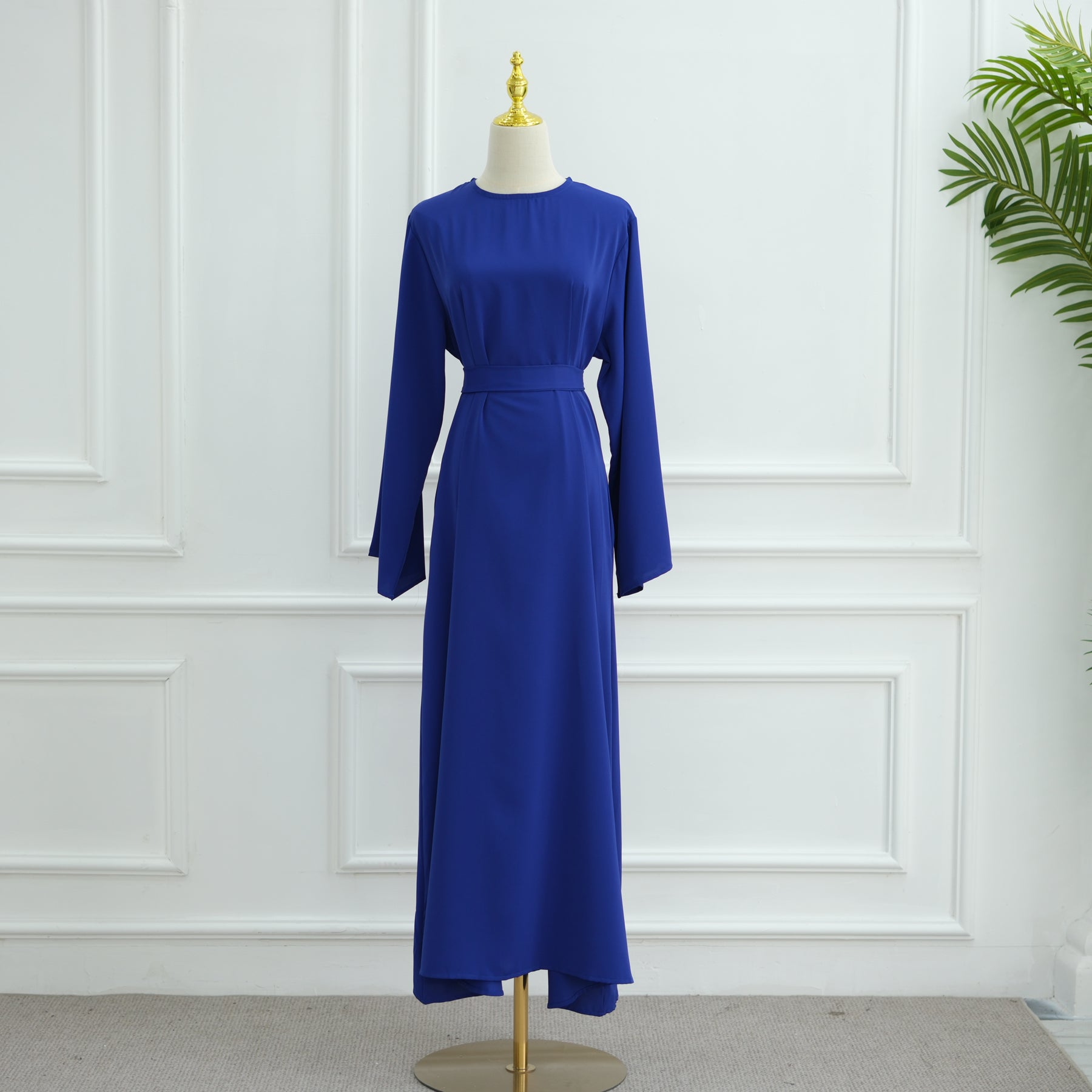 Blue dress on a mannequin against a white paneled wall. AsasAbayaInnerDress_Noor_GraceRoyalBlue - Noor & Grace