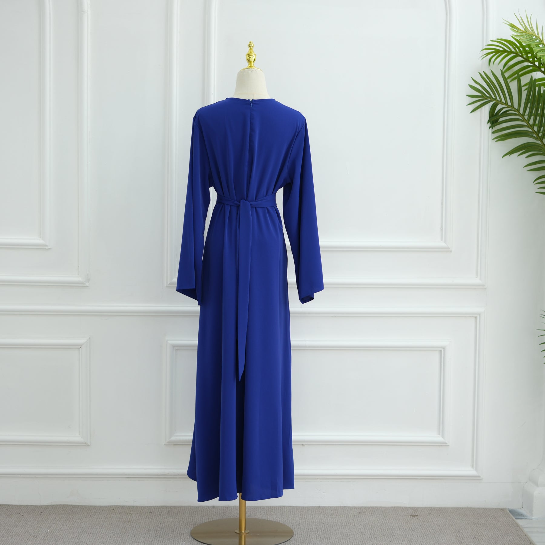 Blue dress on a mannequin against a white paneled wall. AsasAbayaInnerDress_Noor_GraceRoyalBlue - Noor & Grace