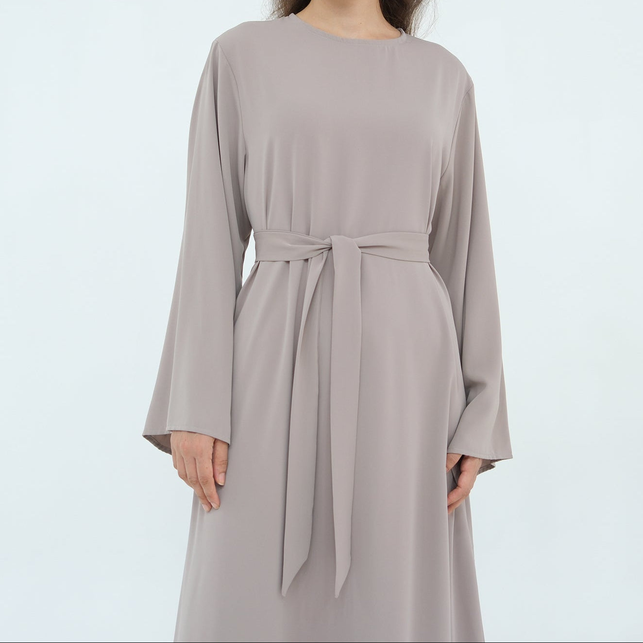 Woman wearing a long-sleeve, long-line dress with a belt on a light gray background
