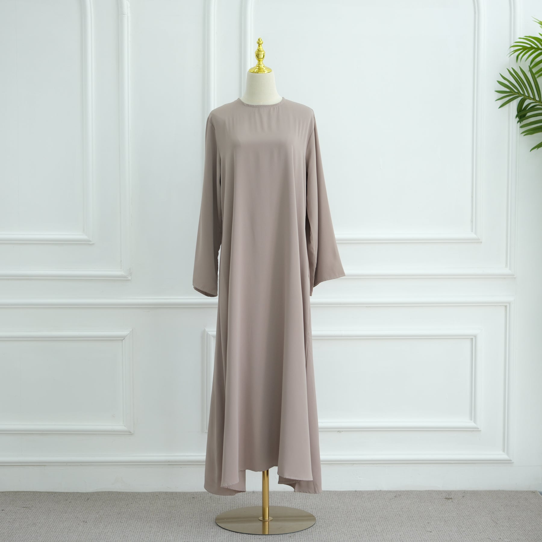 Long beige dress on a mannequin against a white paneled wall. AsasAbayaInnerDress_Noor_GraceTaro - Noor & Grace