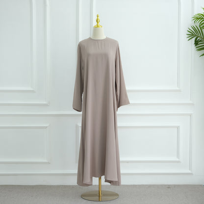 Long beige dress on a mannequin against a white paneled wall. AsasAbayaInnerDress_Noor_GraceTaro - Noor & Grace