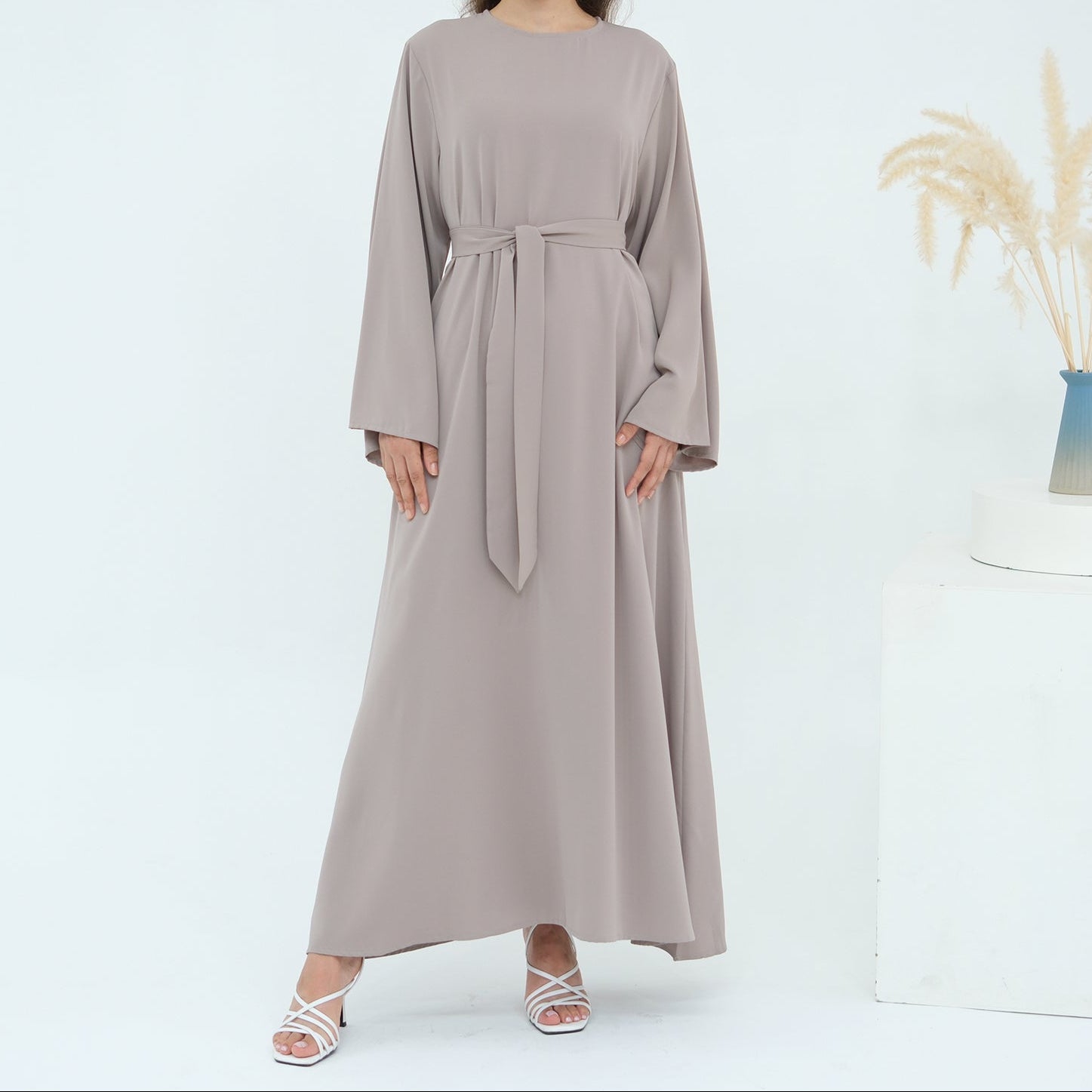 Woman wearing a long beige dress with a belt on a white background