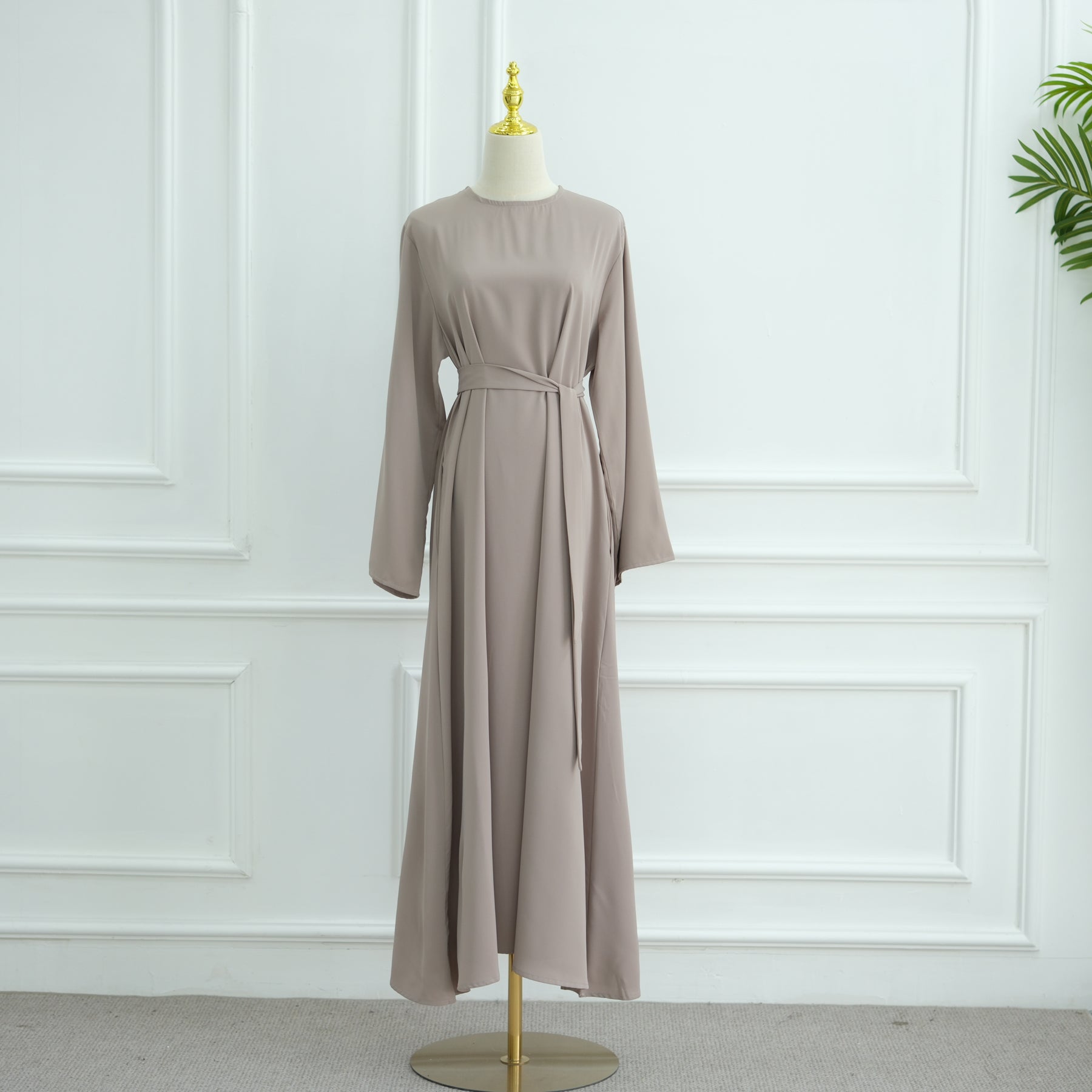 Beige dress on a mannequin against a white paneled wall. AsasAbayaInnerDress_Noor_GraceTaro - Noor & Grace