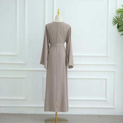 Long beige dress on a mannequin against a white paneled wall. AsasAbayaInnerDress_Noor_GraceTaro - Noor & Grace