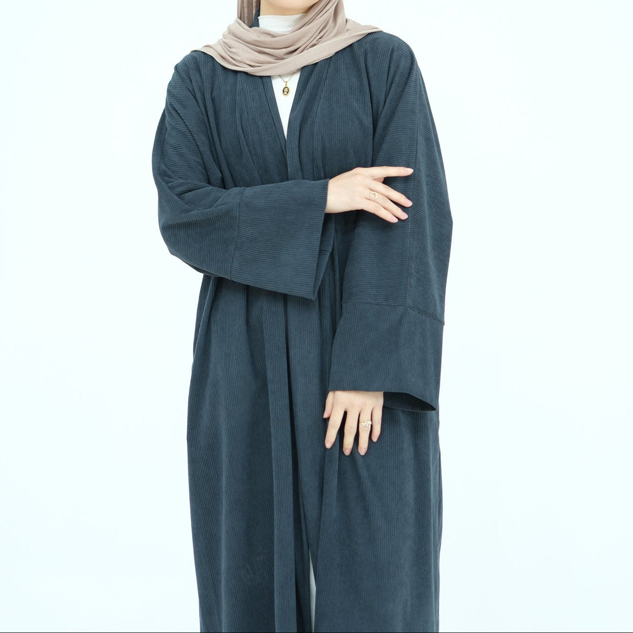 Woman wearing a long dark gray abaya with a beige hijab on a white background. ClassicCorduroyAbaya_Gray1 - Noor & Grace