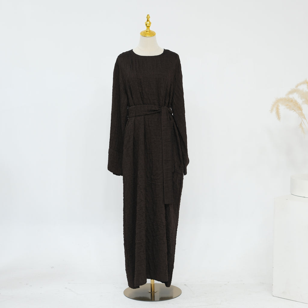 Person wearing a dark brown abaya outfit with a matching headscarf, holding a beige handbag. Dubai_Luxe_2026_Abaya_2026_Coffee_8 - Noor & Grace