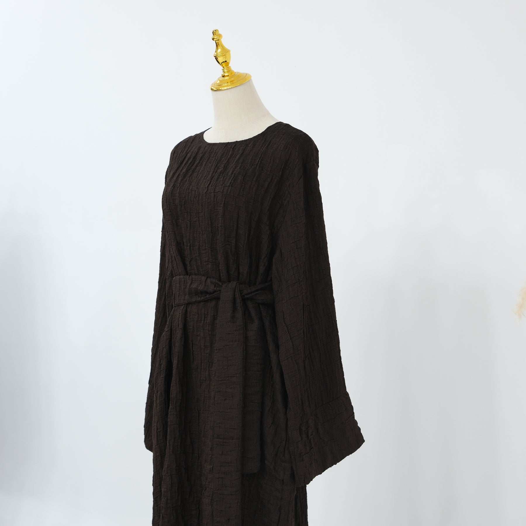 Person wearing a dark brown abaya outfit with a matching headscarf, holding a beige handbag. Dubai_Luxe_2026_Abaya_2026_Coffee_8 - Noor & Grace