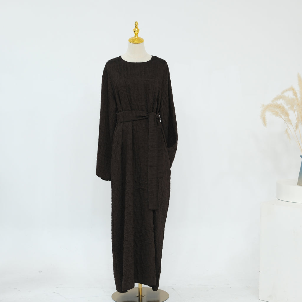 Person wearing a dark brown abaya outfit with a matching headscarf, holding a beige handbag. Dubai_Luxe_2026_Abaya_2026_Coffee_8 - Noor & Grace
