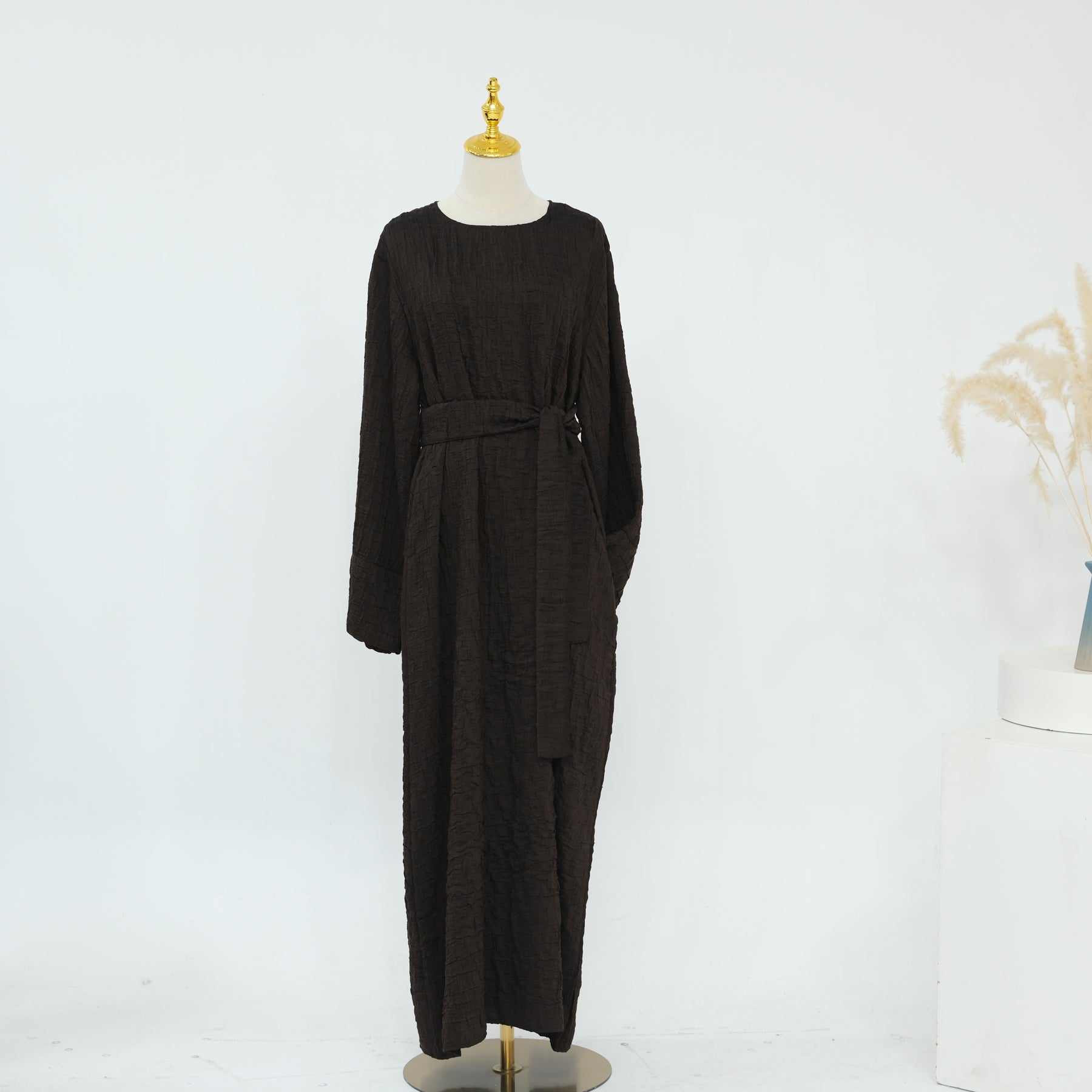 Person wearing a dark brown abaya outfit with a matching headscarf, holding a beige handbag. Dubai_Luxe_2026_Abaya_2026_Coffee_8 - Noor & Grace
