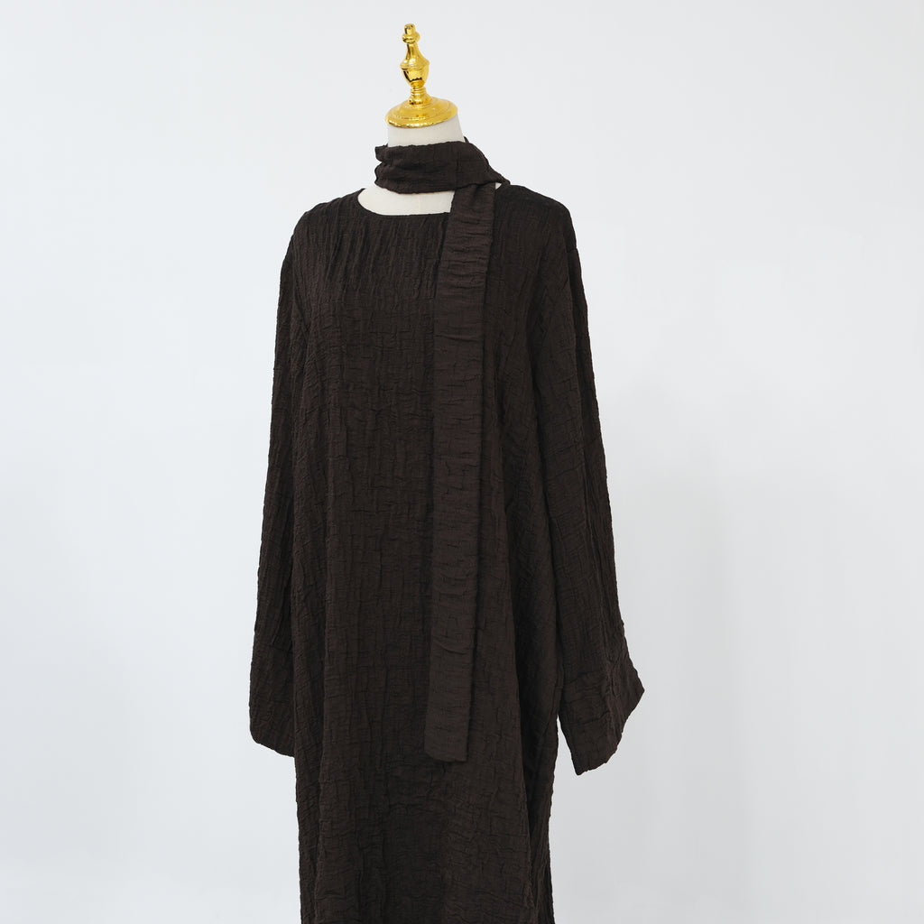 Person wearing a dark brown abaya outfit with a matching headscarf, holding a beige handbag. Dubai_Luxe_2026_Abaya_2026_Coffee_8 - Noor & Grace