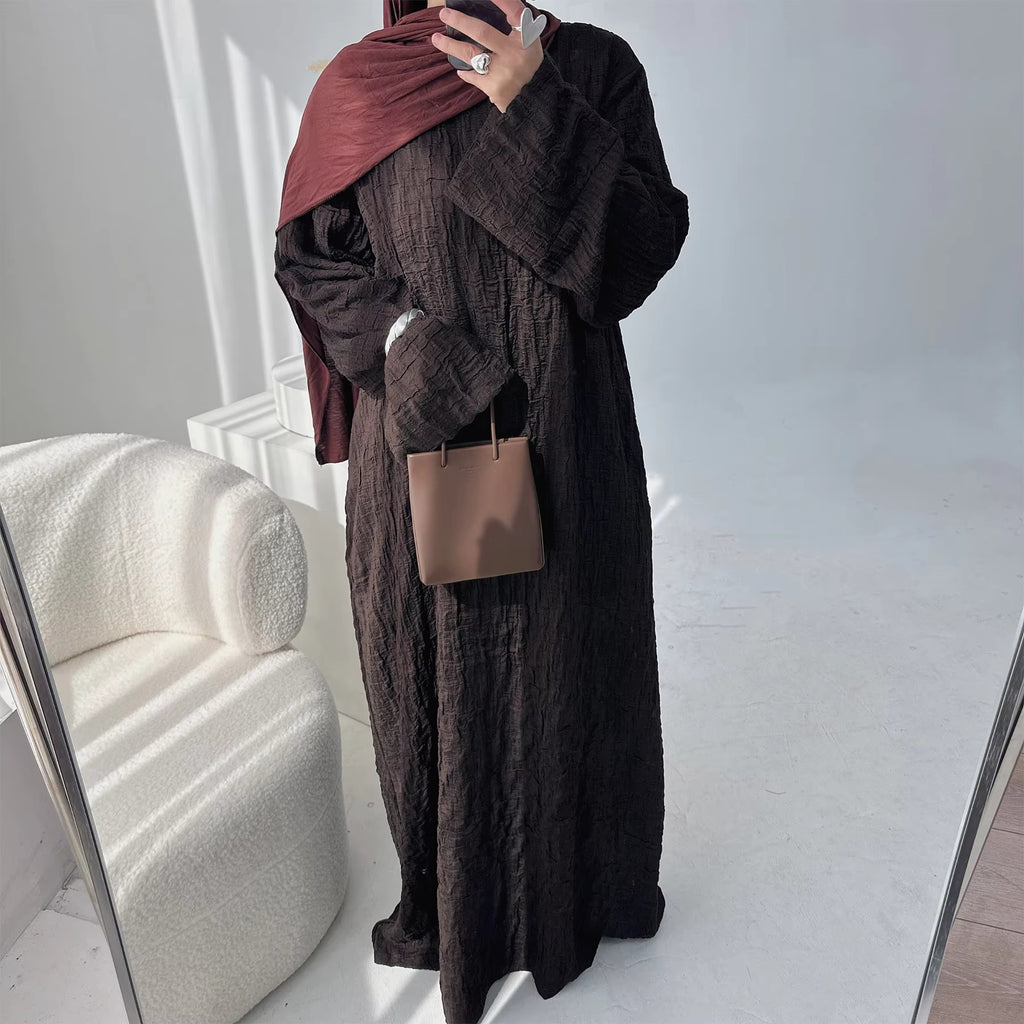 Person wearing a dark brown abaya outfit with a matching headscarf, holding a beige handbag. Dubai_Luxe_2026_Abaya_2026_Coffee_8 - Noor & Grace