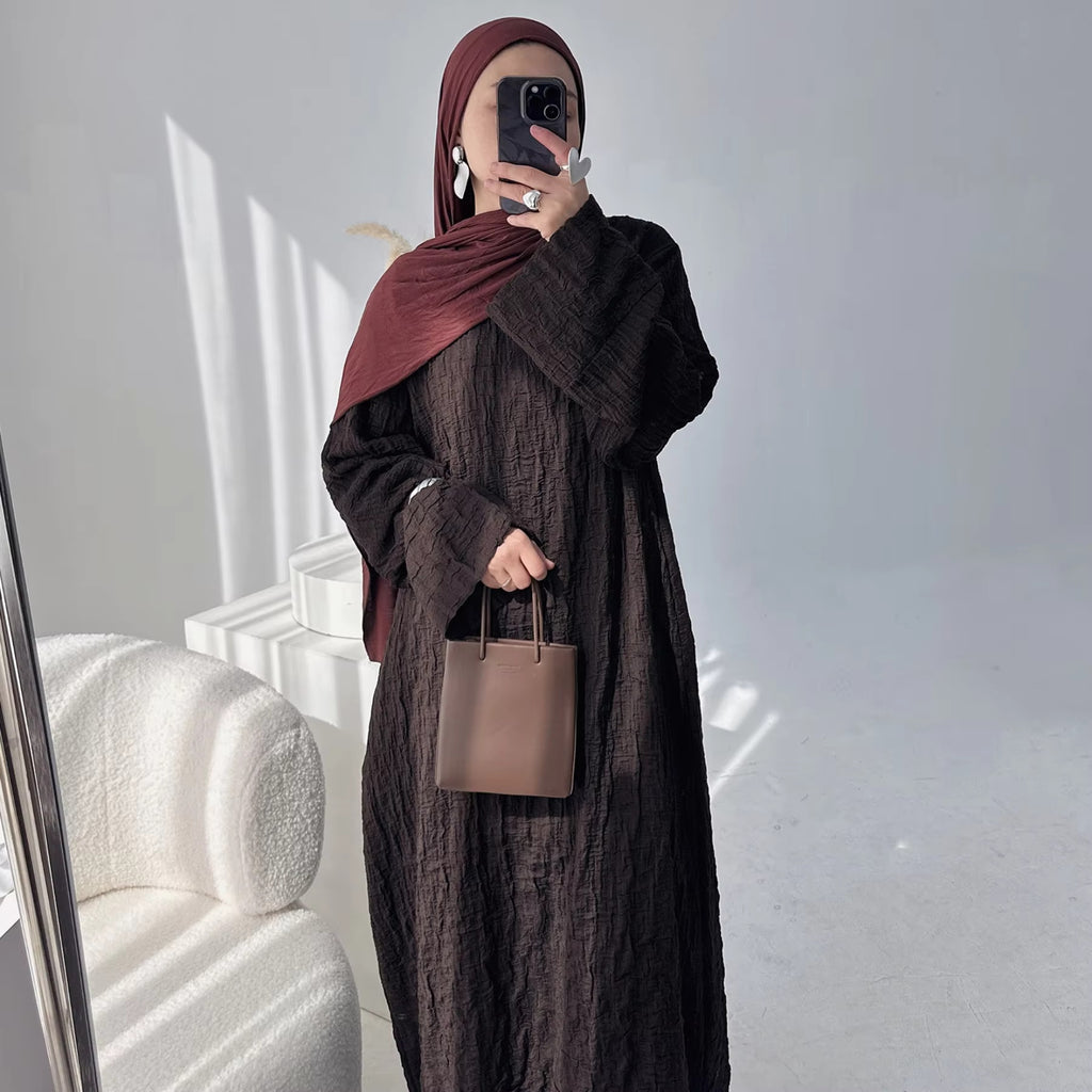 Person wearing a dark brown abaya outfit with a matching headscarf, holding a beige handbag. Dubai_Luxe_2026_Abaya_2026_Coffee_8 - Noor & Grace