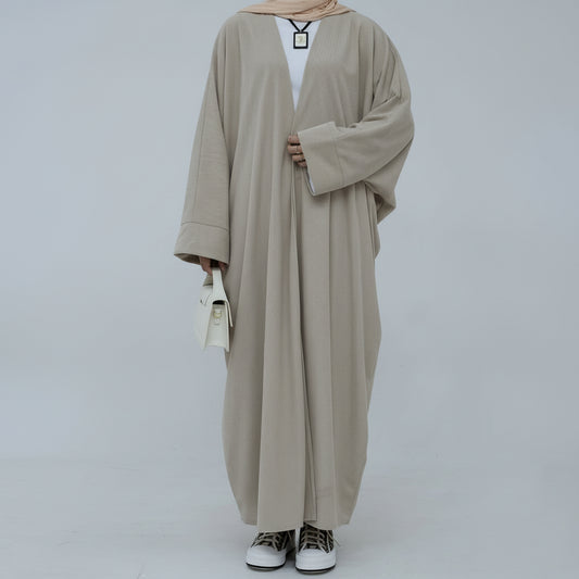 Person wearing a beige corduroy abaya with a white background and a vase with dried plants on the left. EverydayCorduroyAbaya_Beige1 - Noor & Grace