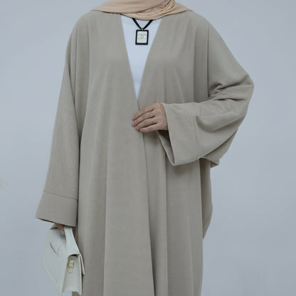Person wearing a beige corduroy abaya with a white background and a vase with dried plants on the left. EverydayCorduroyAbaya_Beige1 - Noor & Grace